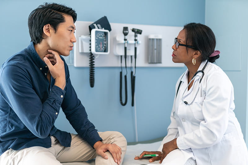 A young man sitting on an exam bed talking to a doctor